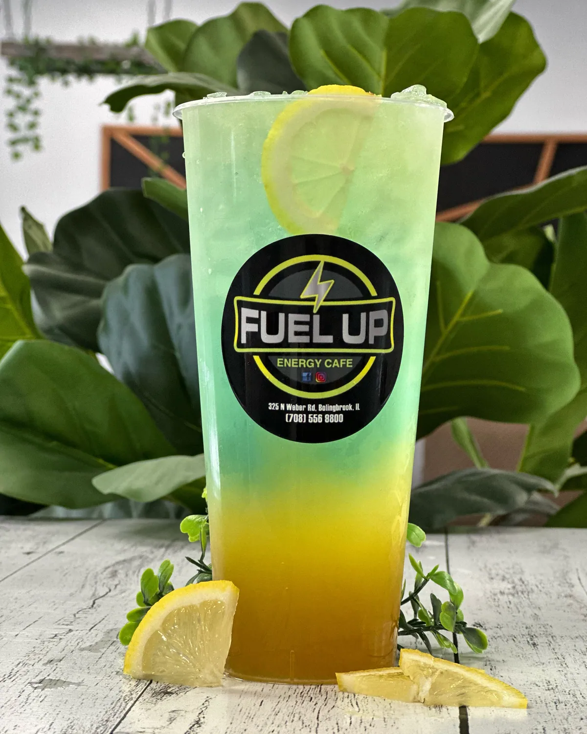 A green and yellow LIT TEA with lemon in front of lush greenery