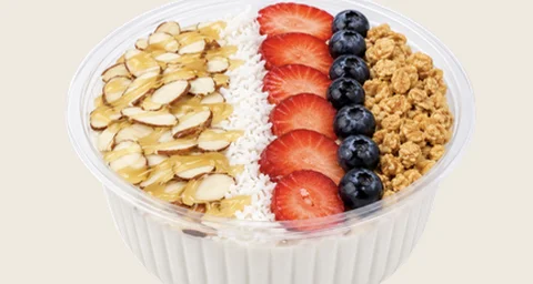 Coconana bowl topped with granola, toasted coconut, slivered almonds, strawberries and blueberries